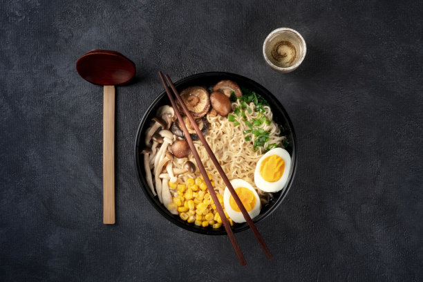拉面。鸡蛋、香菇和蔬菜荞麦面，上面的照片是黑色背景，配以传统的木勺、筷子和一杯清酒图片下载