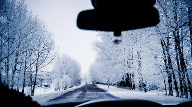 在雪地里行驶在乡间小路上。透过挡风玻璃观看一辆行驶的汽车。道路转弯和路标图片下载