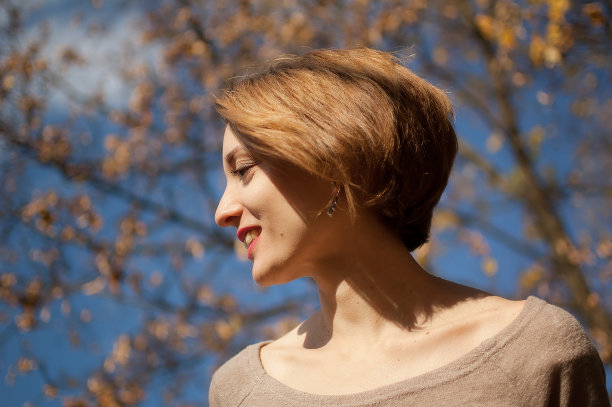 户外肖像的一个美丽的年轻女士短发戴着银色耳环和米色连衣裙摆pose反对蓝色的天空和树木与黄色的树叶背景花时间在秋天的公园图片下载