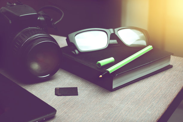 淡绿色的笔放在黑色笔记本上，智能手机和带记忆卡的数码相机放在木桌上。自由职业者旅行者摄影师笔记。图片下载