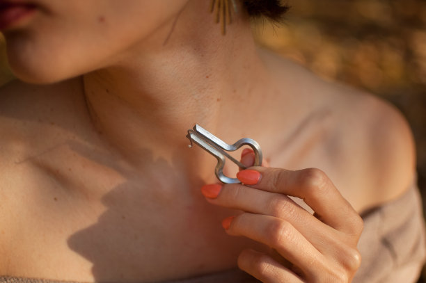 近距离的户外照片的年轻女性萨满在米色衣服裸露的脖子和肩膀持有传统的hutsul drymba，下巴的竖琴，银色的vargan在手里。图片下载