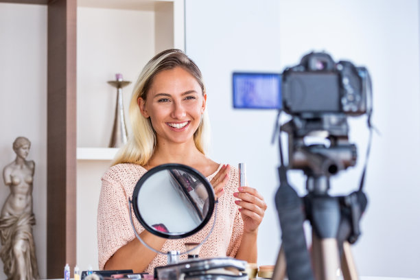 年轻的女士谈论化妆品拿着化妆调色板而录制她的视频。一个女人在为她的化妆品博客制作视频。图片下载