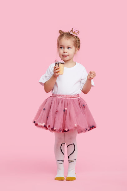 可爱的小女孩愉快地吃着美味的冰淇淋在一个粉红色的工作室背景。闭着眼睛舔。婴儿食品和快乐童年的概念图片下载