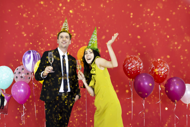 年轻夫妇拿着酒杯，在红色背景下庆祝。图片下载