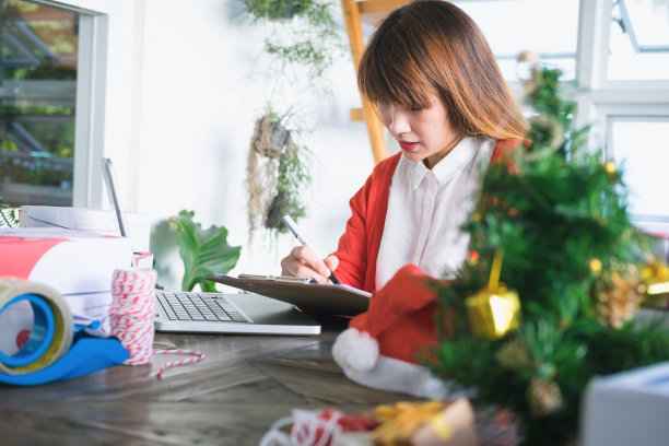 美丽年轻的亚洲企业主与电脑和tabet微笑而站在车间。回复商务电子邮件，撰写客户订单的产品订单。图片下载