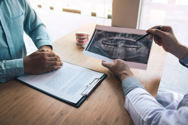 牙医手持笔指点x光照片，并与患者谈论药物和手术治疗。图片下载