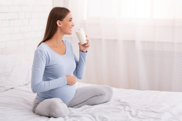 孕妇坐在家里的床上喝牛奶图片下载