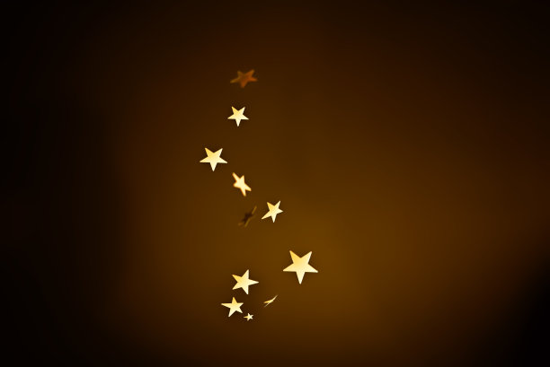 金色的星星五彩纸屑落在深棕色的背景上。图片下载