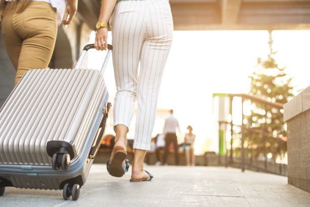 两个金发碧眼的年轻女孩拿着行李箱出现在一家豪华酒店的背景上。带着行李度假的游客的朋友图片下载