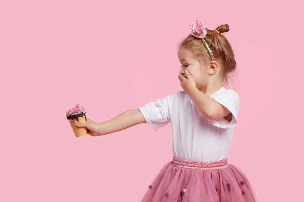 可爱的小女孩把冰淇淋放在他伸出的手臂上，用手捂住他的嘴。在粉色的画室背景下拒绝吃无味的甜点。正确的婴儿食品不含糖图片下载