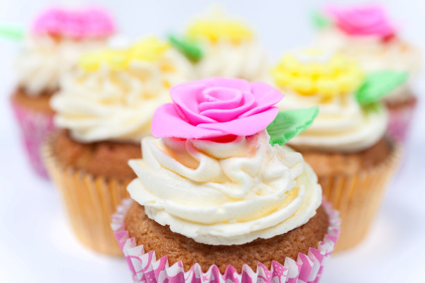 有糖霜或糖霜的纸杯蛋糕，粉红色、黄色和奶油色的绿叶、玫瑰和花卉装饰的白色背景照片图片下载