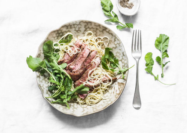 意大利扁面，切片牛肉和火箭沙拉在一个轻的背景，俯视图图片下载