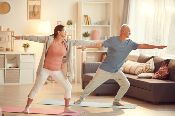 活跃的成熟夫妇穿着运动服站在客厅的运动垫上，伸展手臂，一起练习瑜伽图片下载