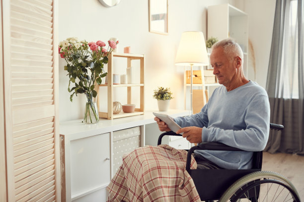 严肃的老年人穿着毛衣，双腿裹着，坐在轮椅上，用平板电脑搜索自己的受伤信息图片下载