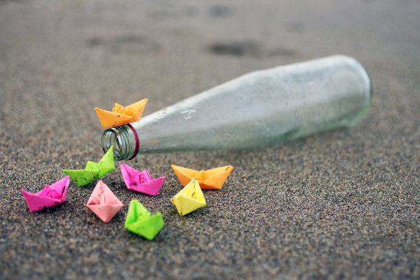 纸船上的透明瓶子概念在海沙上。图片下载