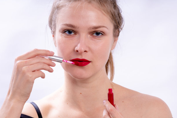 一个美丽的年轻女孩的特写肖像画她的嘴唇与明亮的红色口红看在一个白色的背景上的相机图片下载