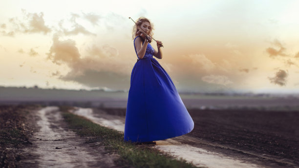 身着长裙的年轻女子的身影带着小提琴在夕阳下的田野里，从事音乐艺术的女孩，对自然的表演，对音乐的概念激情图片下载