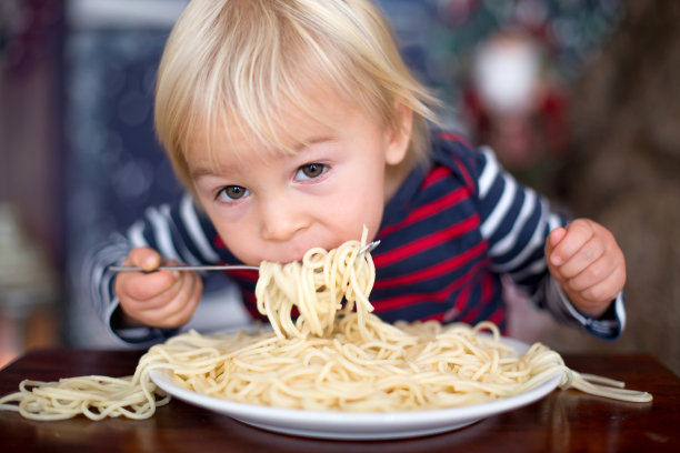 可爱的蹒跚学步的孩子，在家里吃意大利面图片下载