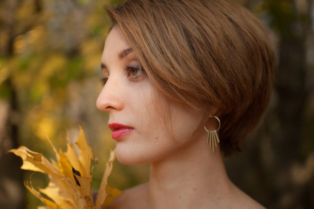 侧视图有吸引力的年轻女子与金发短发持有一束秋天的叶子在一个美丽的红金色秋天公园户外图片下载