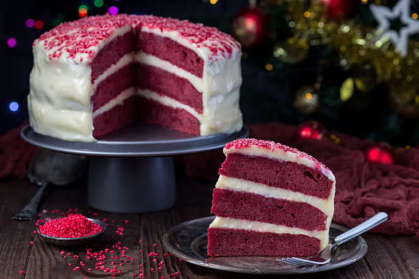 一块自制的红色天鹅绒蛋糕，奶油芝士糖霜在金属盘上，低调的照片与boke灯和圣诞装饰的背景，水平图片下载