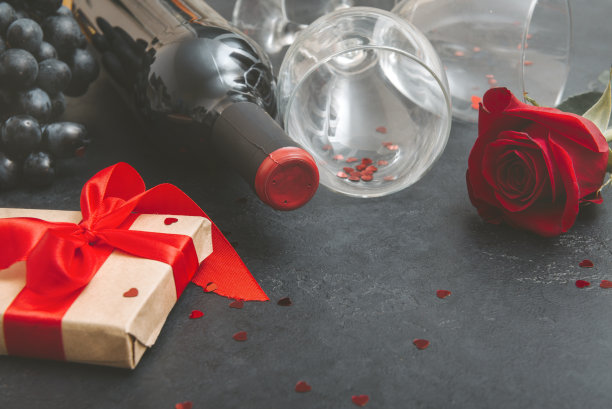 一瓶葡萄酒，2杯，1朵红玫瑰，带丝带的礼盒，深色葡萄，黑色背景上的心图片下载