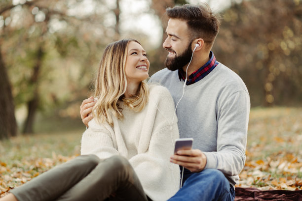 在秋天公园里，情侣们一边玩一边用手机听音乐图片下载