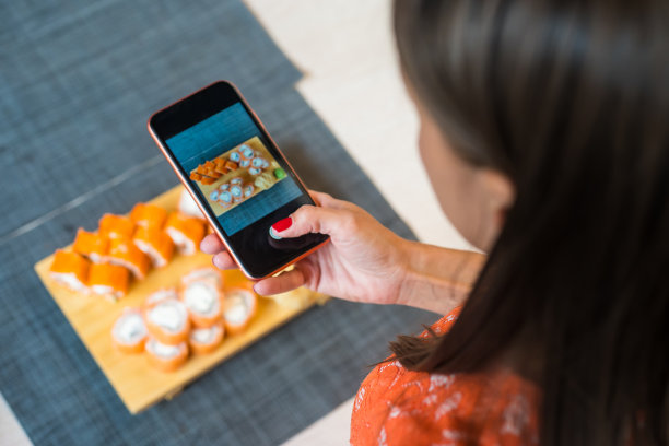 女孩用手机拍寿司。一个女孩正在用放在黑色木桌上的手机拍摄寿司图片下载