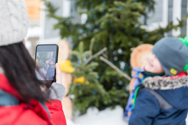 妈妈在室外拍她儿子在圣诞树旁的照片图片下载