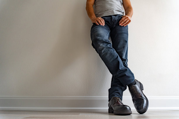 一个穿着黑色牛仔裤，穿着棕色新鞋的野蛮男人站在停车场的白地板旁，等待着有人。图片下载