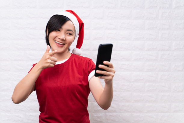 快乐的女人戴着圣诞老人帽，用智能手机图片下载