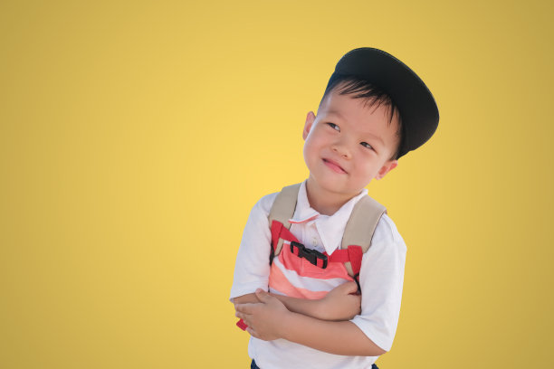 亚洲蹒跚学步的小男孩微笑着双臂交叉，在彩色背景和剪接路径上思考，第一天在学校/回到学校的概念图片下载