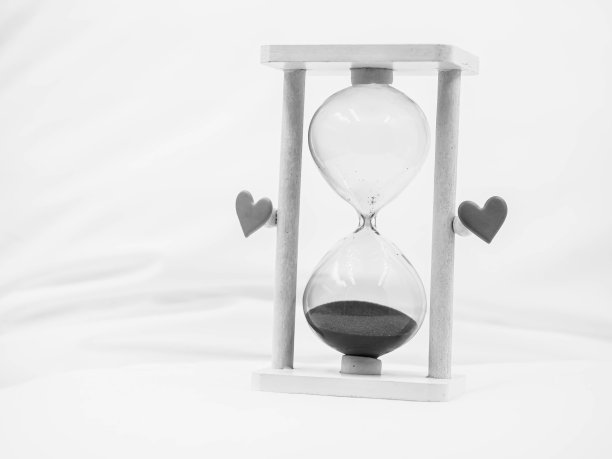 黑白色调。卧室里模糊皱巴巴的被单上有沙漏和心形贴纸的特写。离婚、分手、悲伤、孤独、黑暗、爱情和时间的观念和观念。图片下载