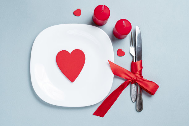 情人节餐桌设置有盘子，叉子，刀，礼盒和红色的心，在蓝色桌布背景顶视图拷贝空间。图片下载