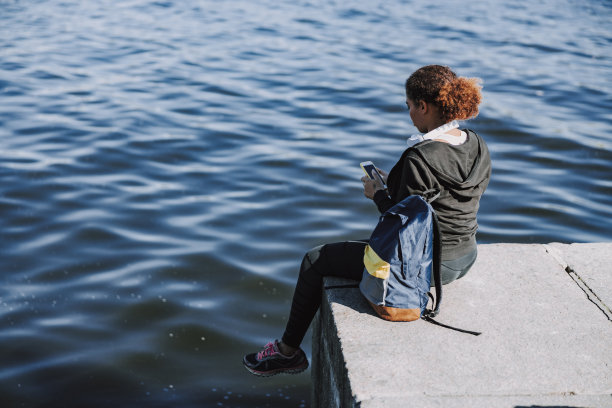 一位美国黑人女士拿着手机坐在河边图片下载