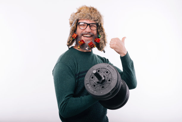 照片中的兴高采烈的男子装饰着胡子，戴着冬季帽子，翘着大拇指，拿着哑铃图片下载