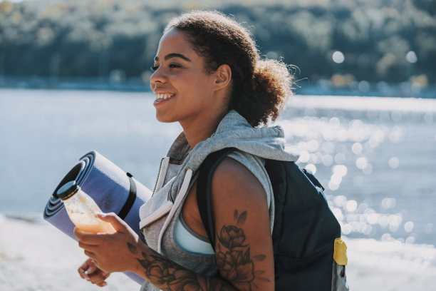 快活的美国黑人女士拿着瑜伽垫和一瓶果汁图片下载