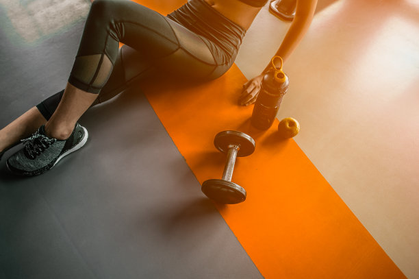 健身女士运动后放松，在健身房旁边放一个乳清蛋白和哑铃。坐在健身房看别处的漂亮年轻女人。图片下载