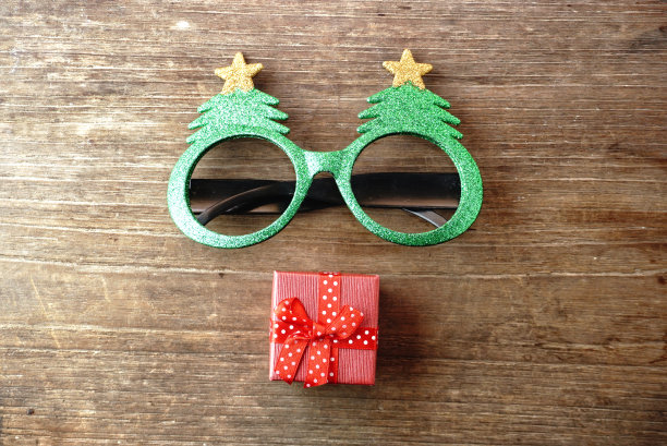奇特的眼镜为圣诞主题装饰与小红色礼品盒的背景木桌。图片下载