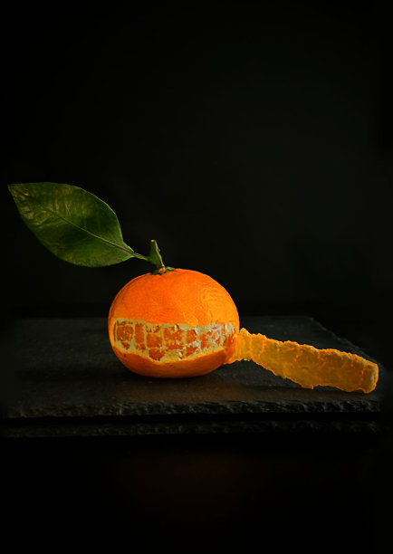 黑色背景的石头桌上放着一个多汁的橘子。普通话开始剥皮。Copyspace图片下载