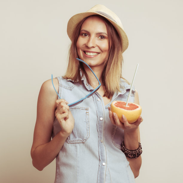 戴着帽子的快乐女人拿着太阳镜和葡萄柚图片下载