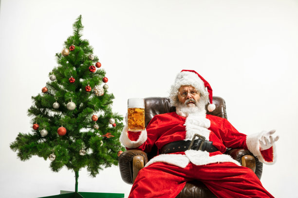 圣诞老人在圣诞树旁喝啤酒，祝贺2020年新年图片下载