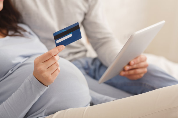 一对怀孕夫妇用数码平板电脑和信用卡在网上购物。图片下载