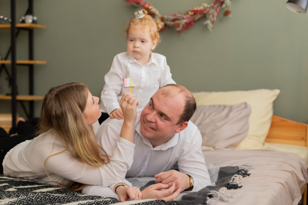 幸福的家庭在现代床上小女儿喂爸爸糖果图片下载