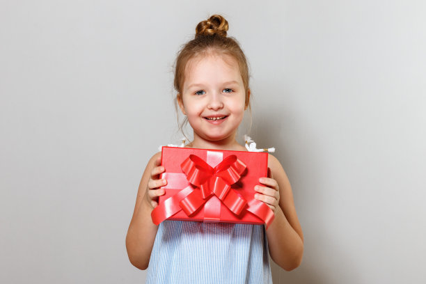 一个可爱的小女孩与礼物盒的特写。灰色背景上的婴儿图片下载
