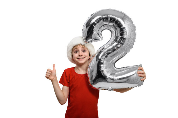 戴着圣诞老人帽子的男孩手中拿着银色的二号充气球。白色背景。图片下载