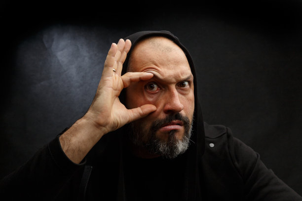 一个戴着黑色兜帽的光头男子的肖像，背景是肮脏的灰色。搜索概念。图片下载