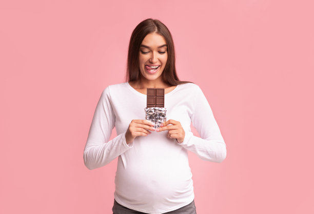 怀孕女孩拿着巧克力站在粉红色的背景，工作室拍摄图片下载