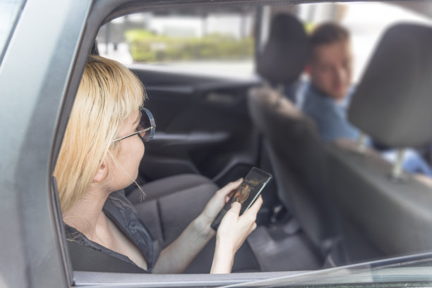 年轻女子在车里与司机交谈，并在手机上查看信息。图片下载