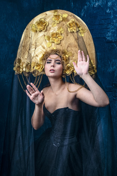 穿着黑色礼服，戴金色帽子的完美女人。美丽的时尚模特在蓝色背景图片下载