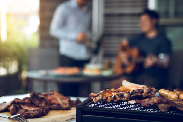 靠近烤架上的烤肉和各种食物，庆祝朋友们在家里弹吉他唱歌。图片下载